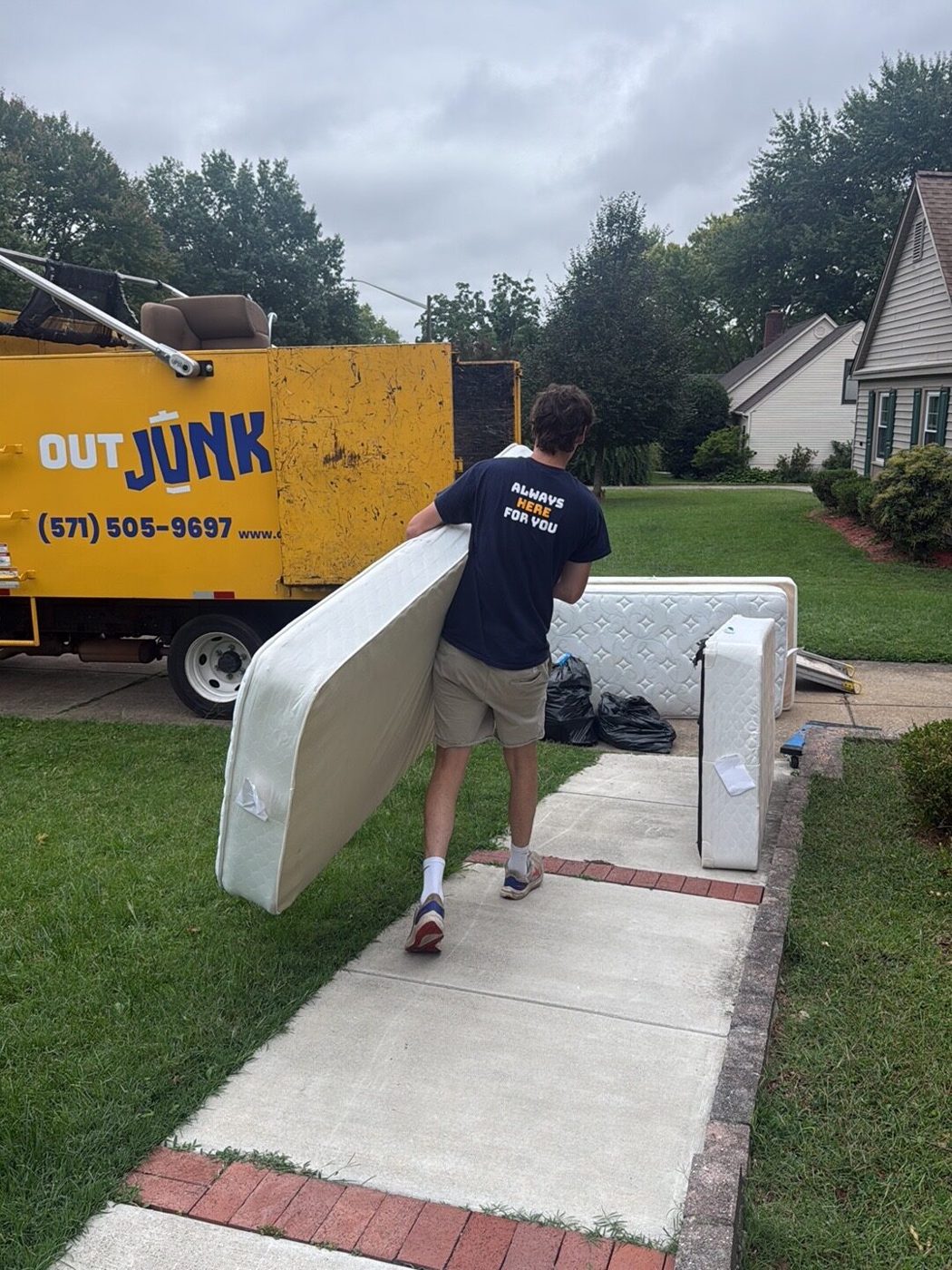 Out Junk Out worker carrying a mattress beside a yellow removal truck